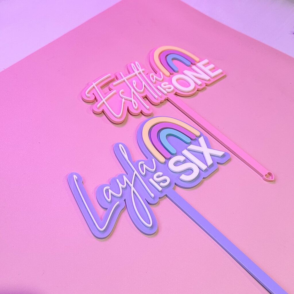 A custom, handcrafted, and personalised cake topper made of layered, frosted, and mirrored acrylic, featuring a rainbow.