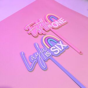 A custom, handcrafted, and personalised cake topper made of layered, frosted, and mirrored acrylic, featuring a rainbow.