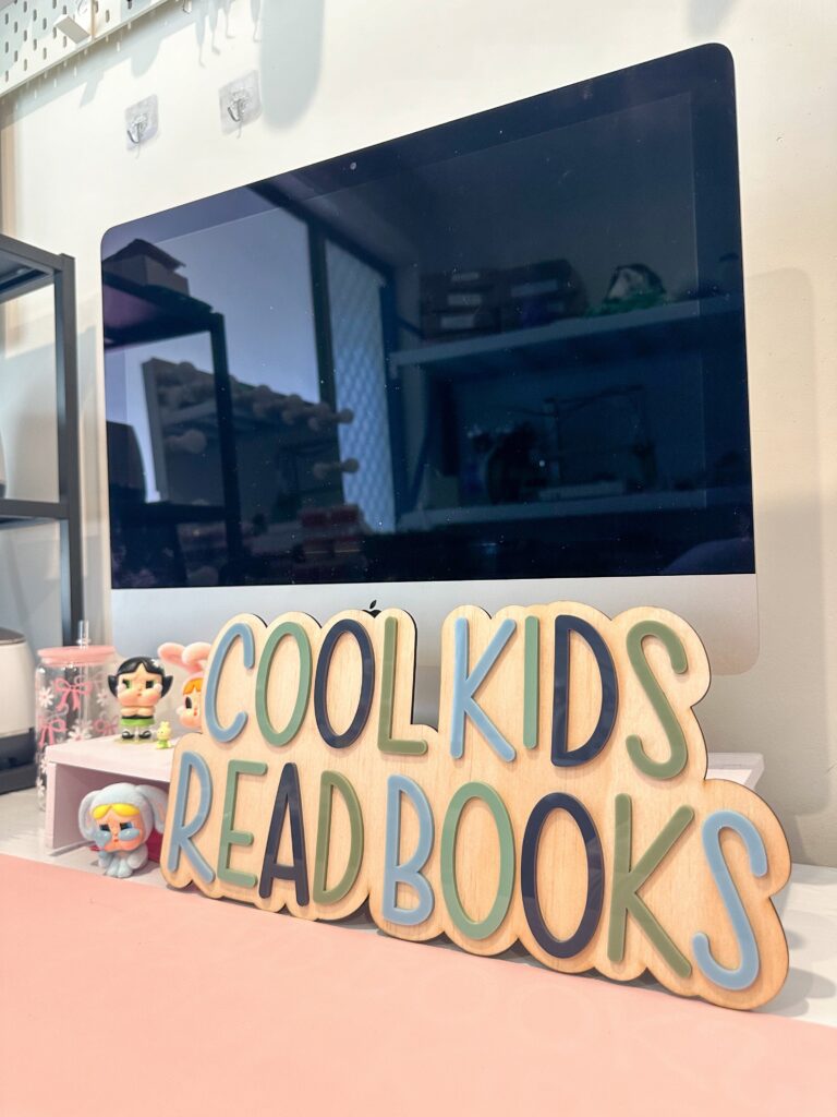 A custom, handcrafted, acrylic and plywood sign that reads "Cool Kids Read Books". The sign features a layered acrylic.
