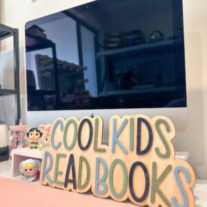 A custom, handcrafted, acrylic and plywood sign that reads "Cool Kids Read Books". The sign features a layered acrylic.