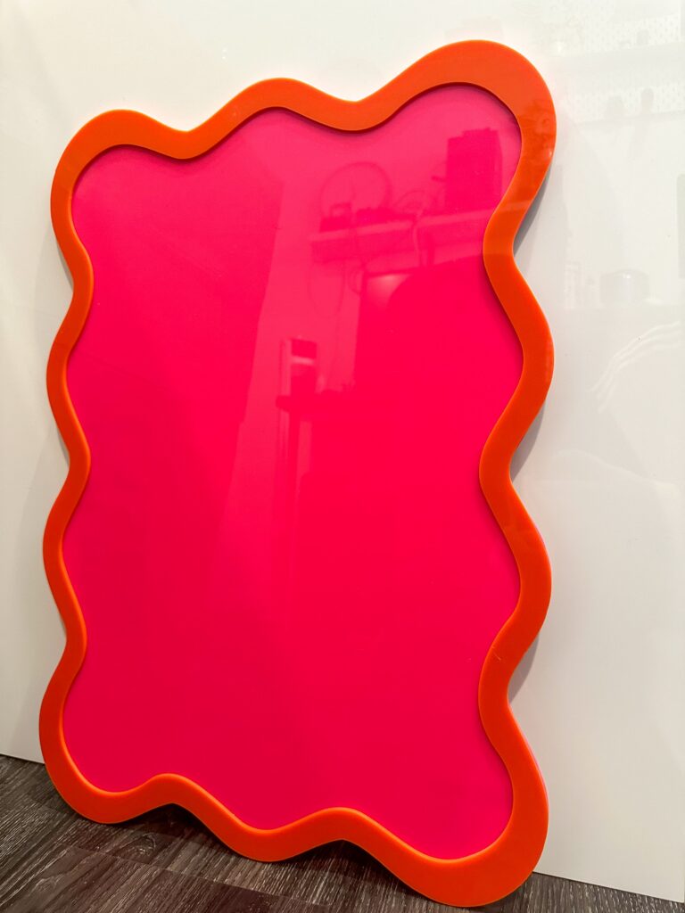 A custom, handcrafted, wave-shaped event board sign made from layered, multi-coloured, and frosted acrylic, with a border.