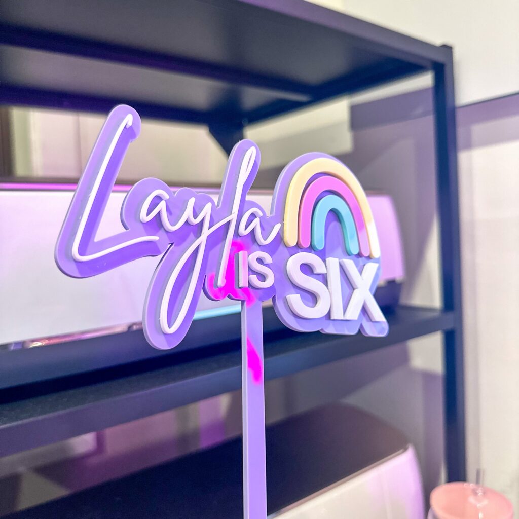 A custom, handcrafted, and personalised rainbow cake topper made from layered acrylic with a custom name and age.