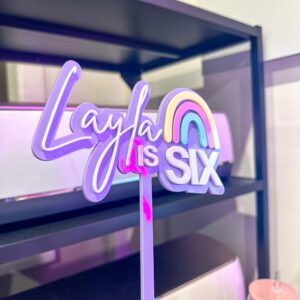 A custom, handcrafted, and personalised rainbow cake topper made from layered acrylic with a custom name and age.