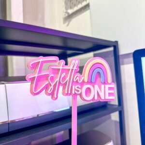 A custom, handcrafted, and personalised rainbow cake topper with a custom name and age, made from layered acrylic.