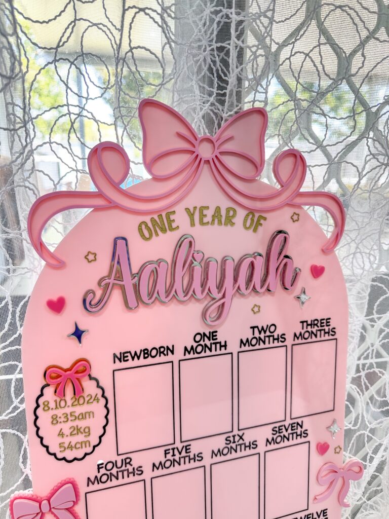 Acrylic photo board with a bow theme, personalised with a name, ideal for capturing a child's first year milestones.