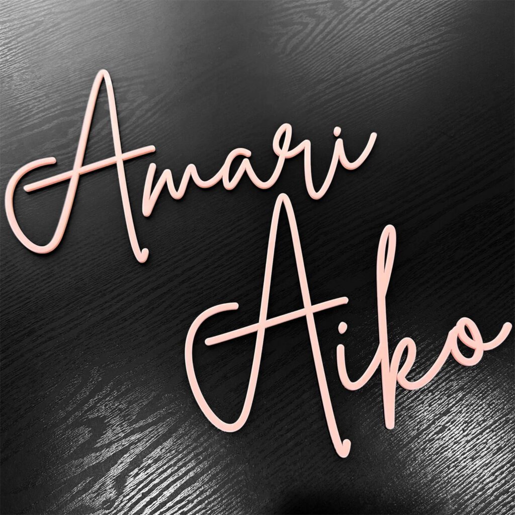 A baby pink acrylic name sign in a single-layer design, featuring names in pretty pink script lettering