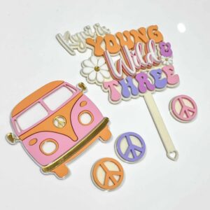 A layered acrylic cake topper with a custom design, featuring the phrase "Young, Wild & Three" in a bold, playful font.