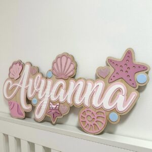 Personalised layered acrylic mermaid name plaque 'Aryanna' with starfish, seashells and blue bubble accents.