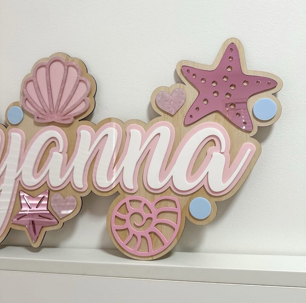 Personalised mermaid name sign 'Ayyanna' with pink seashells, starfish and blue pearl accents on a wooden base.