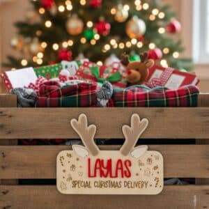 Wooden crate filled with Christmas gifts and plaid blankets with Antler reindeer decoration in front of lit Christmas tree