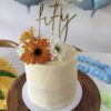 Gold Fifty personalised acrylic cake topper on a white floral celebration cake.